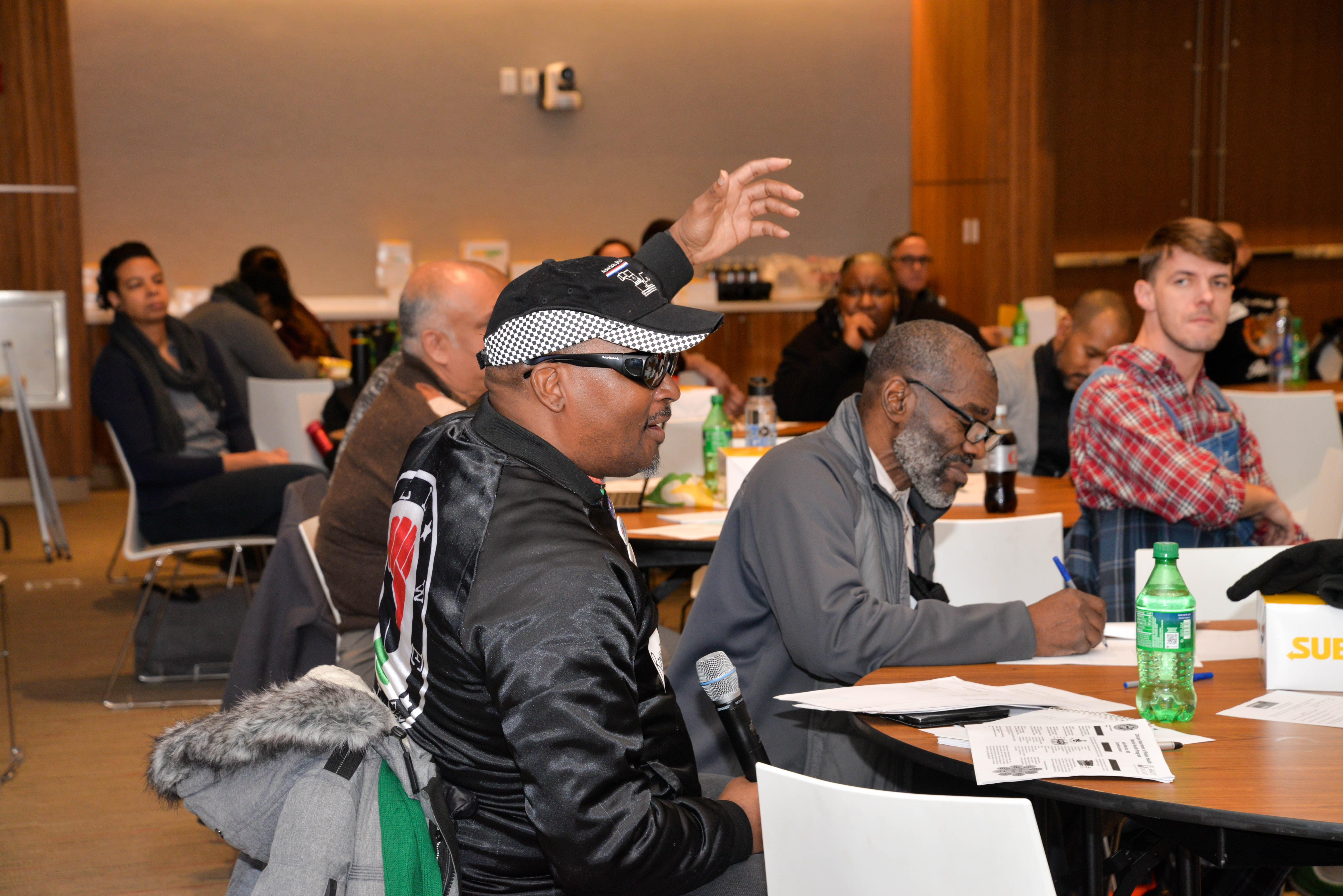 Picture of community member at a town hall raising hand